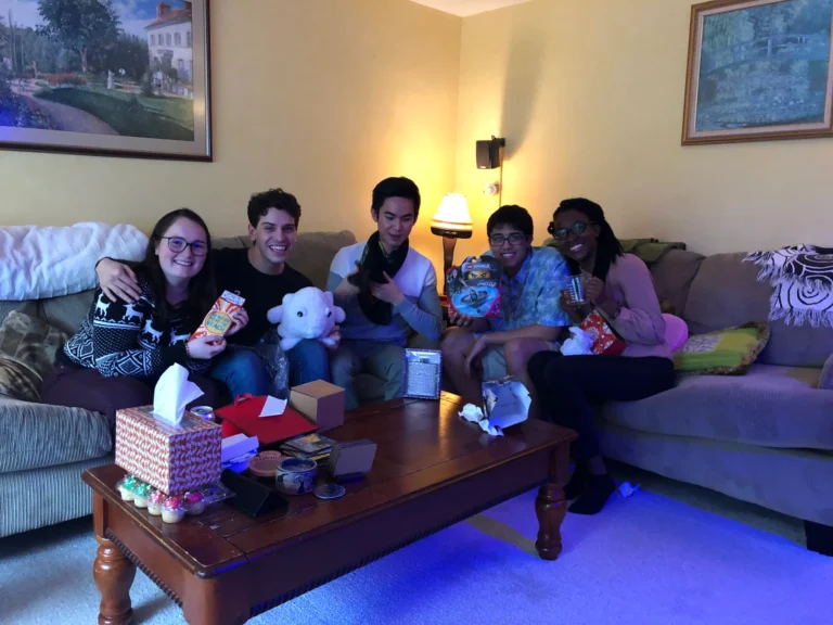 Five Salomon lab members sit together on a sofa, smiling and holding gifts at a group gathering.