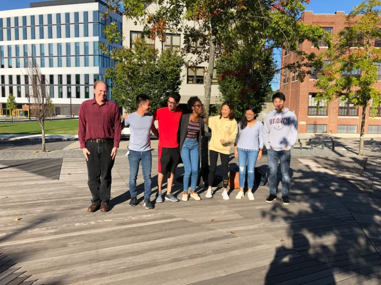 Professor Salomon and six lab members stand together outdoors, smiling and laughing during a group photo.