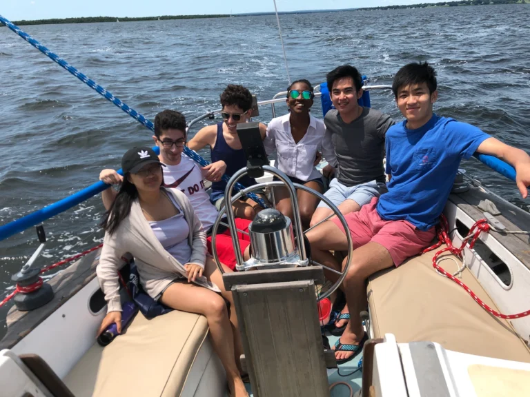 Six Salomon lab members smile together around the helm of a sailboat on the water.
